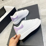 White sneakers with purple accents held by a hand on a black surface.