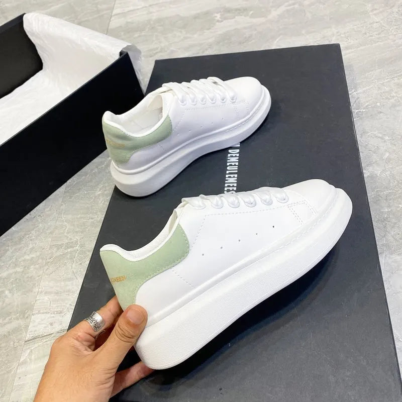 White sneakers with green accents held by a hand on a black surface.