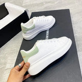 White sneakers with green accents held by a hand on a black surface.