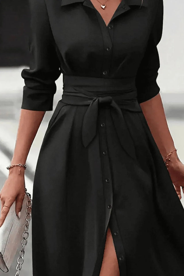 Black dress with a belt and a slit on a neutral background