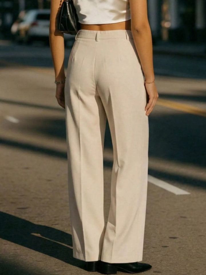Person wearing beige pants and a white top on a street.