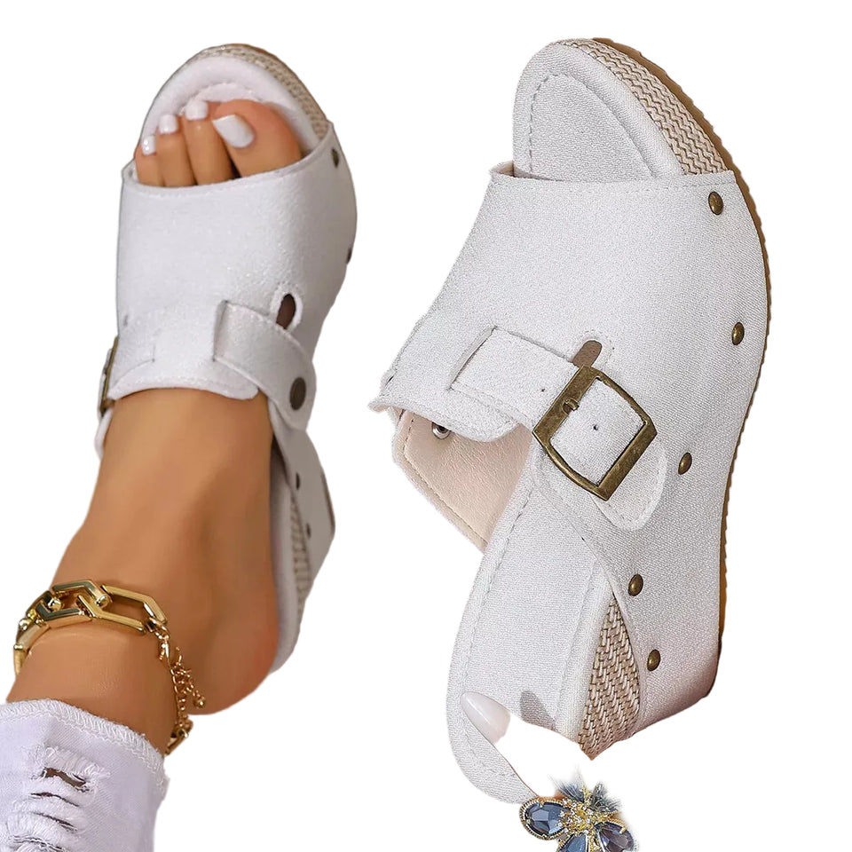 White sandals with buckles worn by a person on a blurred indoor background