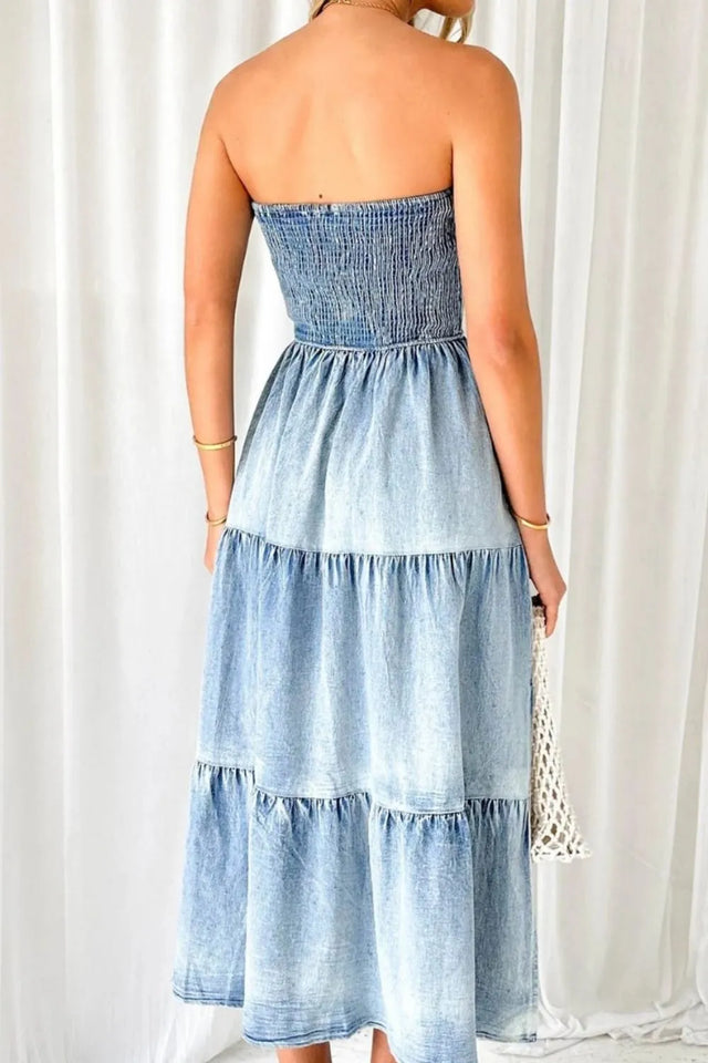 Woman wearing a strapless denim dress against a white curtain background