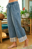 Person wearing blue jeans with lace cuffs in a room with plants and furniture.