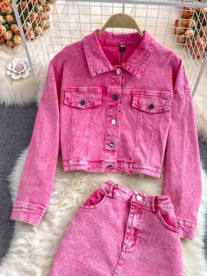 Pink denim jacket and pants set on a textured surface with decorative flowers in the background.