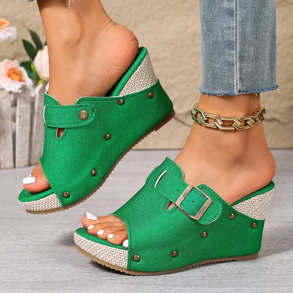 Green wedge sandals worn with denim jeans on a neutral background