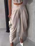 Person wearing beige high-waisted pants and white shoes, holding a small handbag.