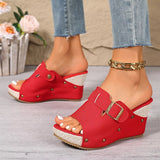 Red wedge sandals with gold buckles worn by a person on a light wooden floor.