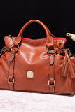 Brown leather handbag with gold accents on a black background