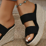Black wedge sandals with jute sole worn by a person on a wooden floor.