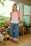 Woman standing in a room with plants and furniture, wearing a pink top and blue jeans.