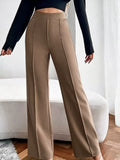 Person wearing beige wide-leg pants with a black top in a room with white curtains.