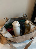 Open beige bag containing a white water bottle, black container, and glass bottle on a light surface.