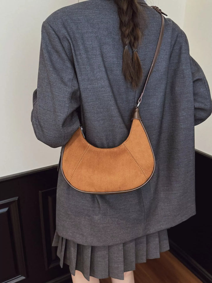 Person wearing a brown leather shoulder bag over their shoulder.
