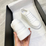 White sneaker with brand logo held by a hand, displayed on a white surface.
