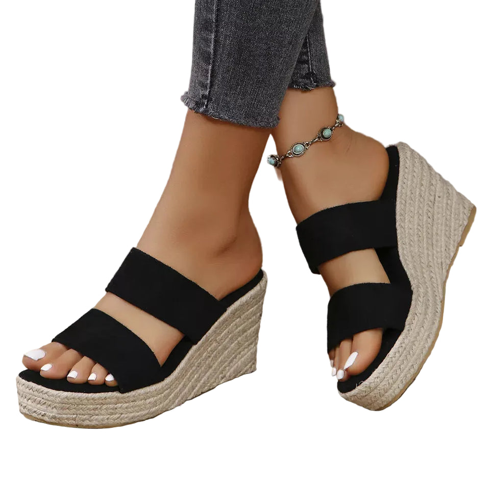 Black wedge sandals on feet with a blurred background
