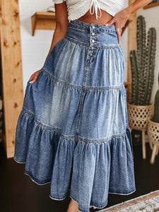 Person wearing a denim dress holding a brown leather bag with a green stone.