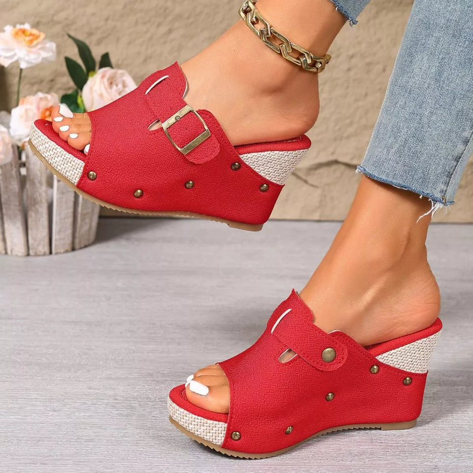 Red open-toe shoes with a buckle worn by a person on a neutral background