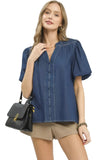 Woman wearing a blue denim blouse with puff sleeves, holding a black handbag on a white background.