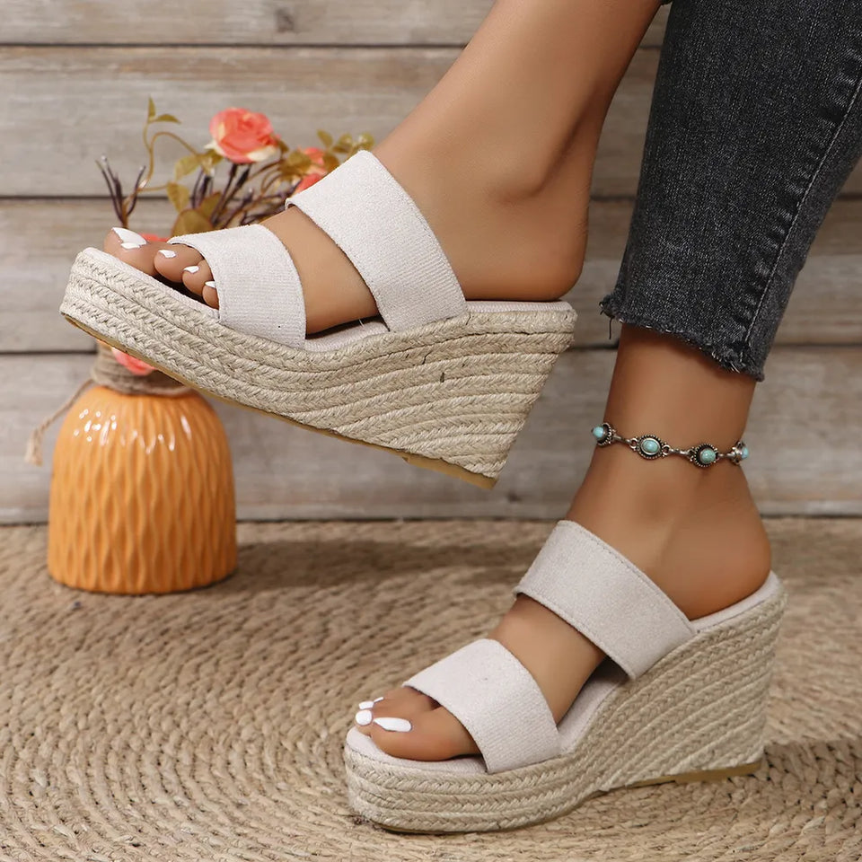 White wedge sandals worn with dark jeans on a wooden floor.