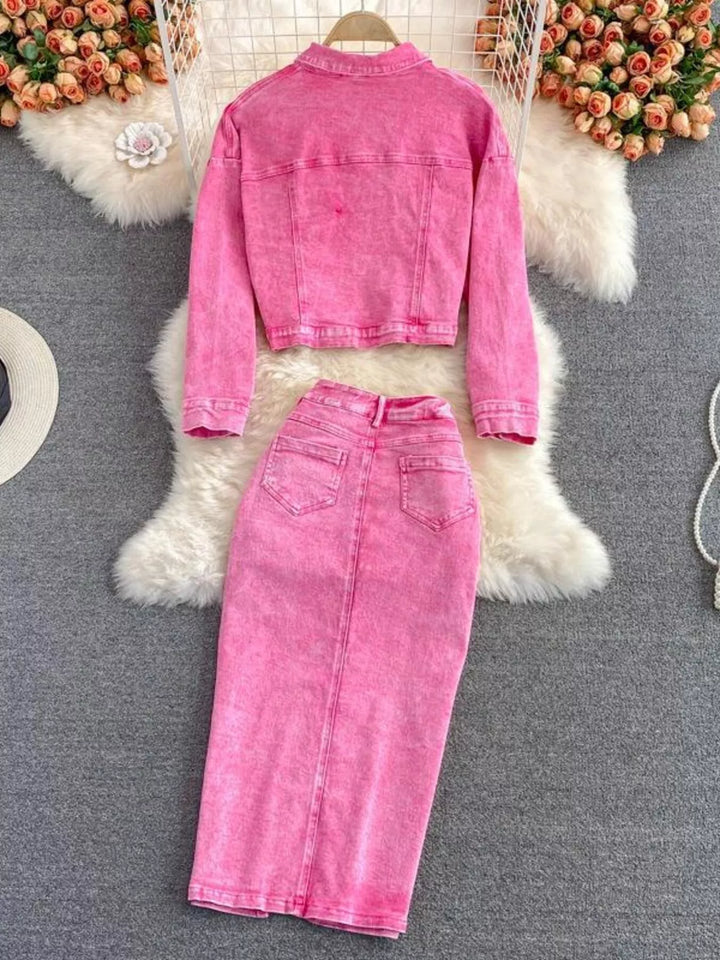 Pink denim jacket and skirt set on a textured surface with floral decorations.