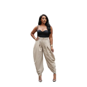 Woman wearing a black top and beige high-waisted pants in an indoor setting with plants.