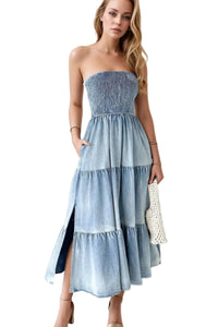 Woman wearing a strapless, tiered denim dress against a white curtain background