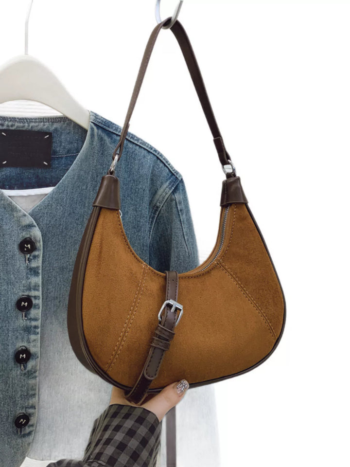 Brown leather handbag held by a person with a denim jacket in the background