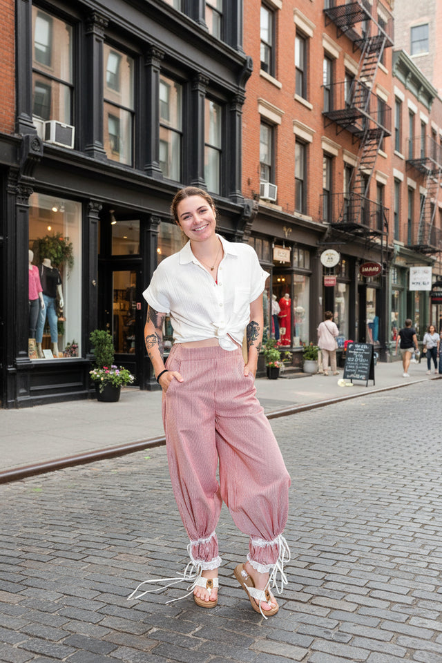 Person wearing a white shirt and pink pants with lace details in a store setting.