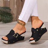 Black open-toe sandals with gold buckles worn by a person on a wooden floor.
