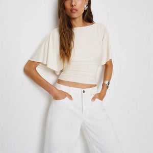 Woman wearing a white crop top and white pants against a plain background