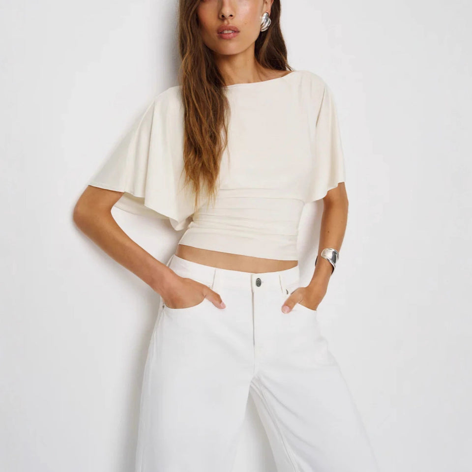 Woman wearing a white crop top and white pants against a plain background