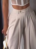 Person wearing a white blouse with sheer panels and beige high-waisted pants, holding a white handbag.